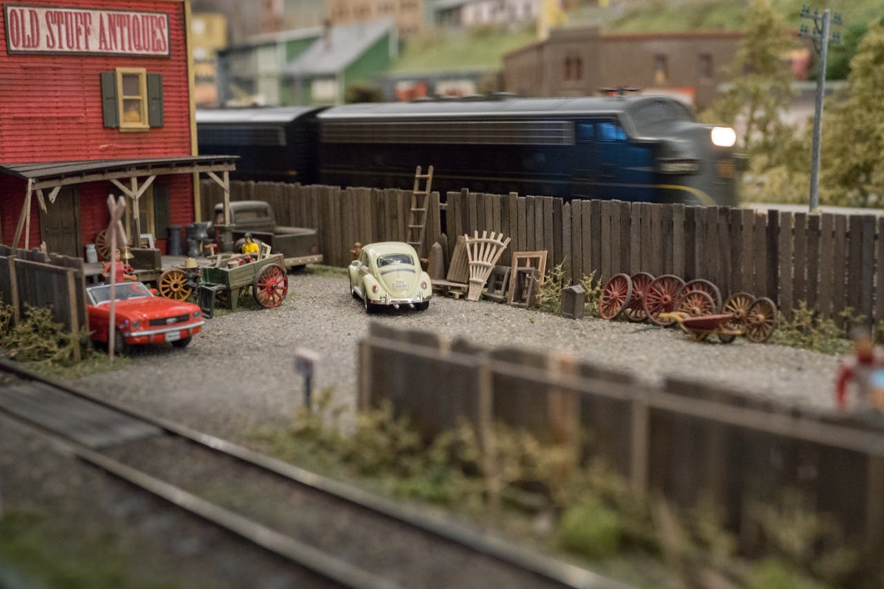 A detailed model train diorama with vintage cars, train, and an antique shop facade.
